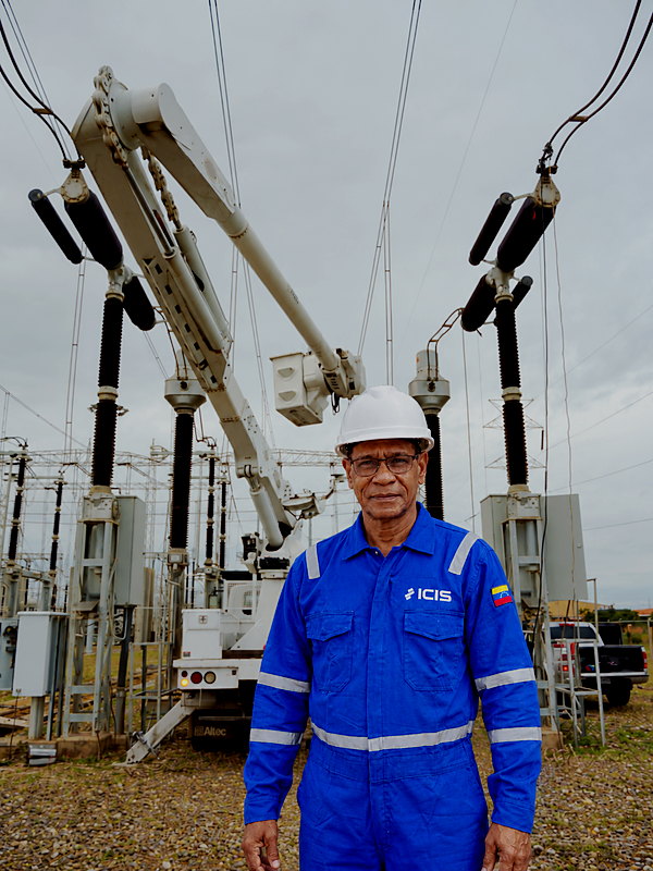 Técnico de Grupo ICIS con uniforme corporativo en patio de subestación, junto a camión canasta y seccionadores de alta tensión