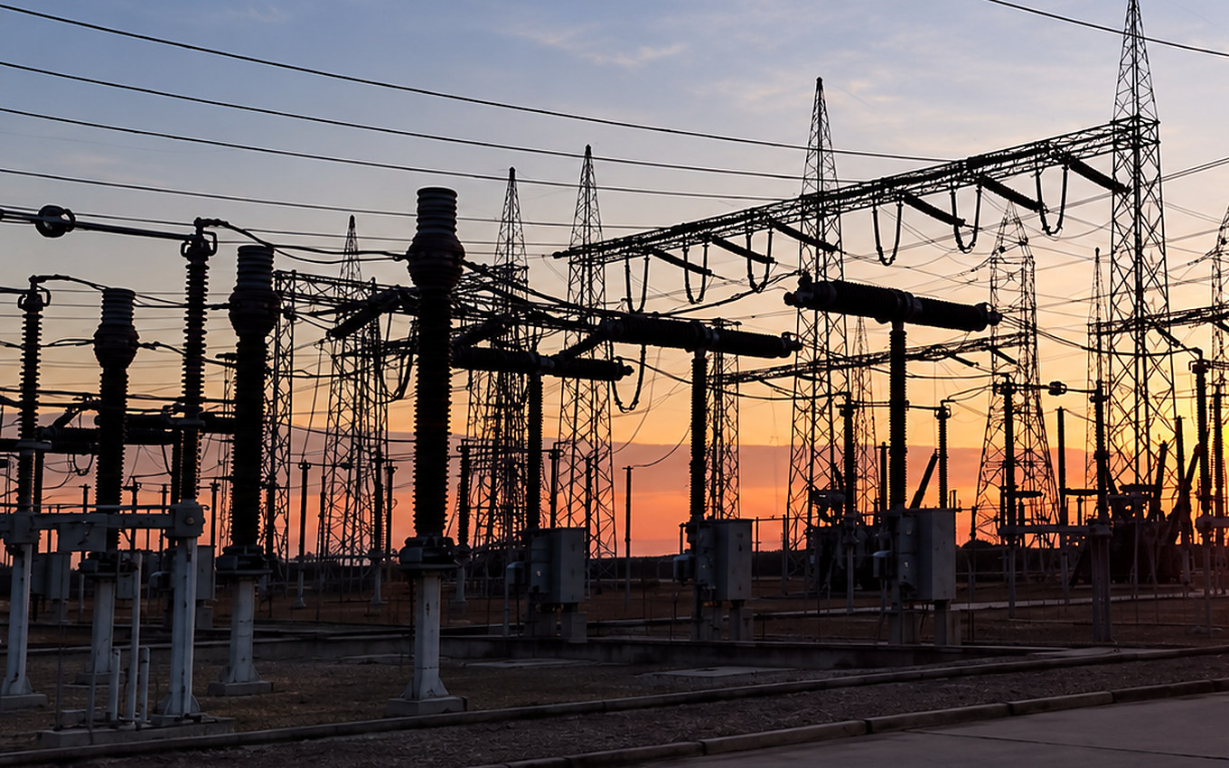 Patio de una subestación de transmisión a contraluz al atardecer, con pórticos, seccionadores y líneas de alta tensión